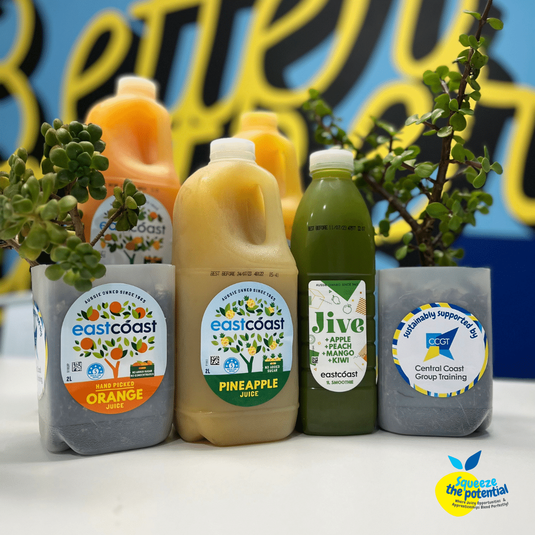 Two Eastcoast Beverage juice bottles have had the top part cut off, and succulents have been planted in them. They sit amongst four other Eastcoast Juices, full of fresh juice and very colourful!